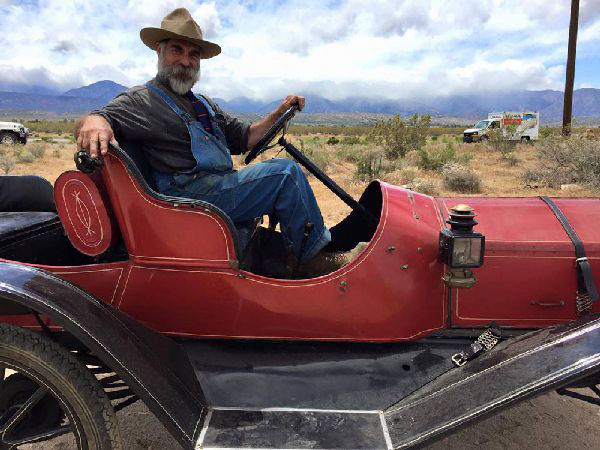 man wearng at hat drives and antique red vehicle
