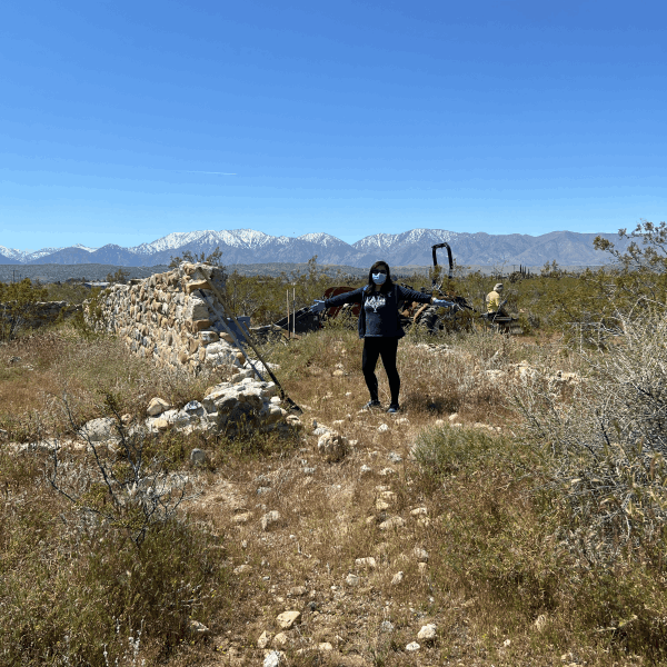 Woman wearing a mask spreads her arms wide next to a ruin