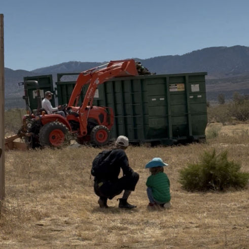 Multigenerational stewardship - father and son look on as an elder tractors trash into a dumpster